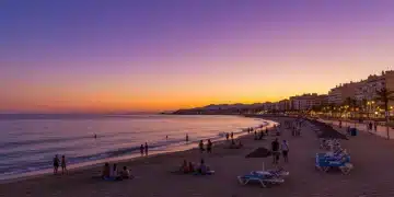 Idílica playa española al atardecer, turistas disfrutando, reflejando el éxito del turismo en España.