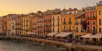 Vista panorámica de una ciudad costera española al atardecer, con turistas disfrutando y edificios históricos, representando el auge del turismo y las oportunidades de inversión.