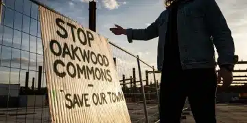 A community organizer gesturing at a weathered protest sign against a construction site at dusk, highlighting local development controversies.